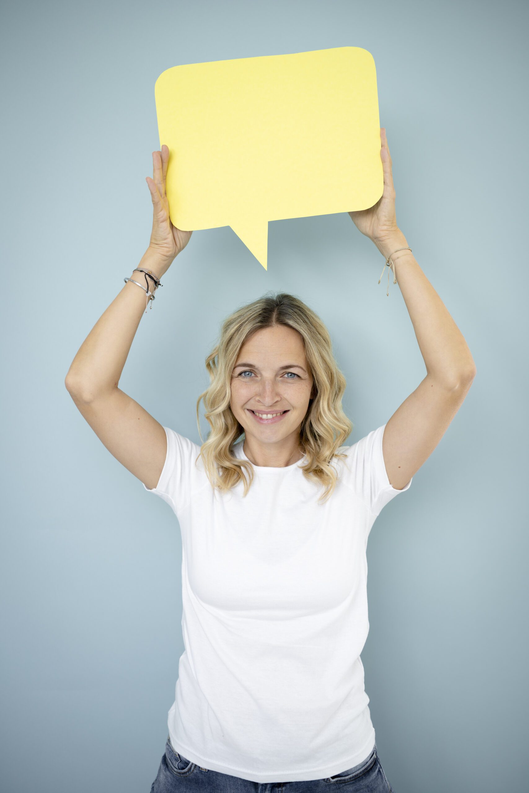 pretty young woman with blonde curls is standing in front of blue wall and holding speech bubble